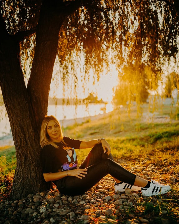Bella ragazza adolescente si siede sotto un albero con un magnifico tramonto sullo sfondo