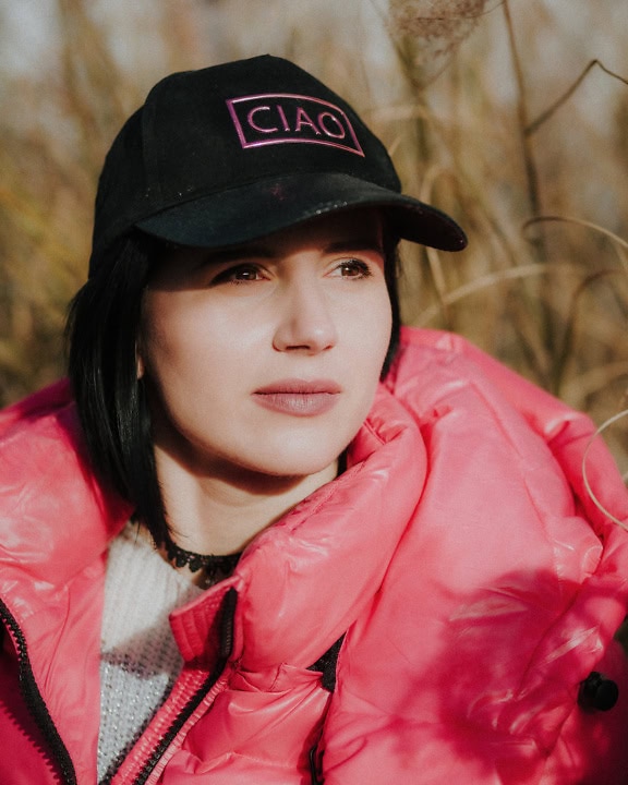 Portrait of a young woman with a delicate beautiful face wearing a black sport’s cap and pink jacket