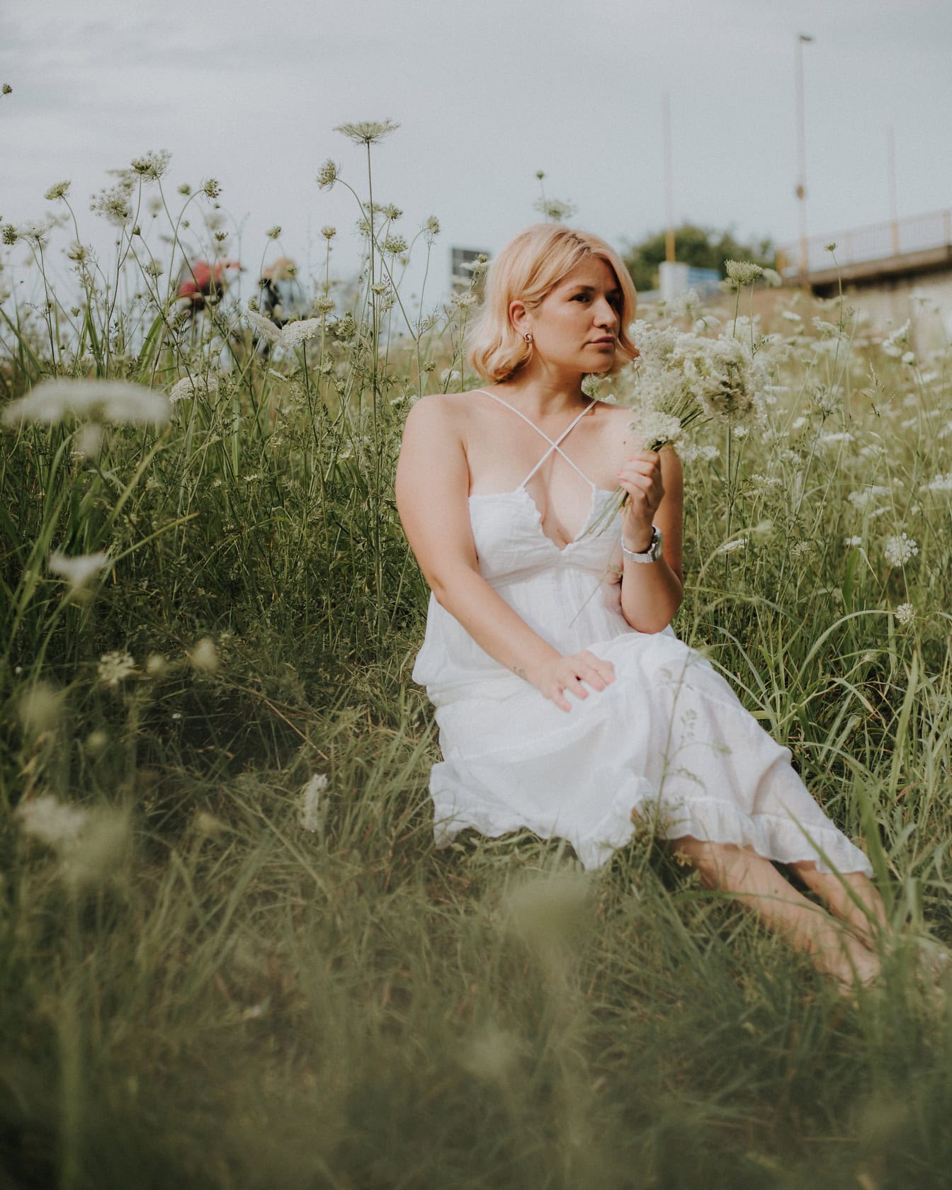 Çiçek tarlasında oturan beyaz kır tarzı gelinlik giymiş güzel bir kadın