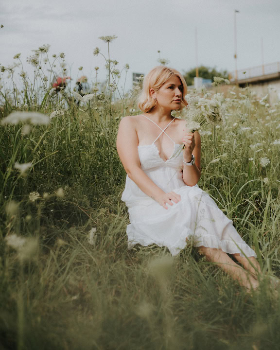 꽃밭에 앉아 있는 화이트 컨트리 스타일 웨딩 드레스를 입은 아름 다운 여자