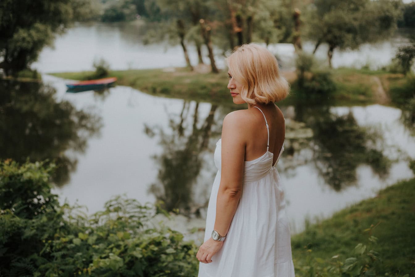 Nevesta v jednoduchých bielych svadobných šatách pózuje pri jazere