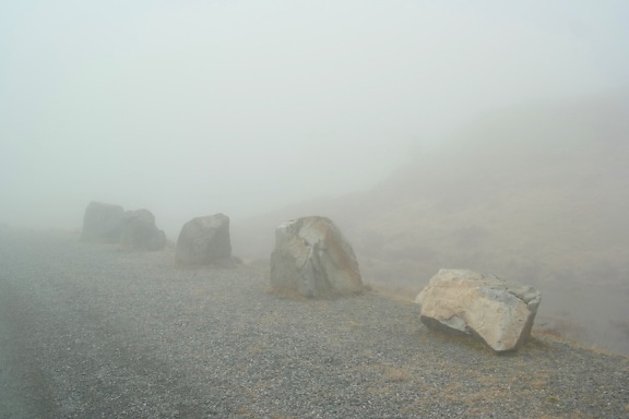 Grandes rocas junto a la carretera en medio de una niebla extremadamente densa