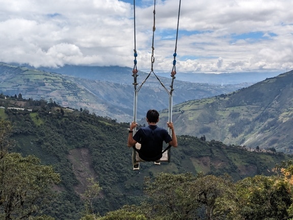 Γενναίος άνθρωπος σε μια μεγάλη κούνια πάνω από την κοιλάδα διάσημο τουριστικό αξιοθέατο στον Ισημερινό