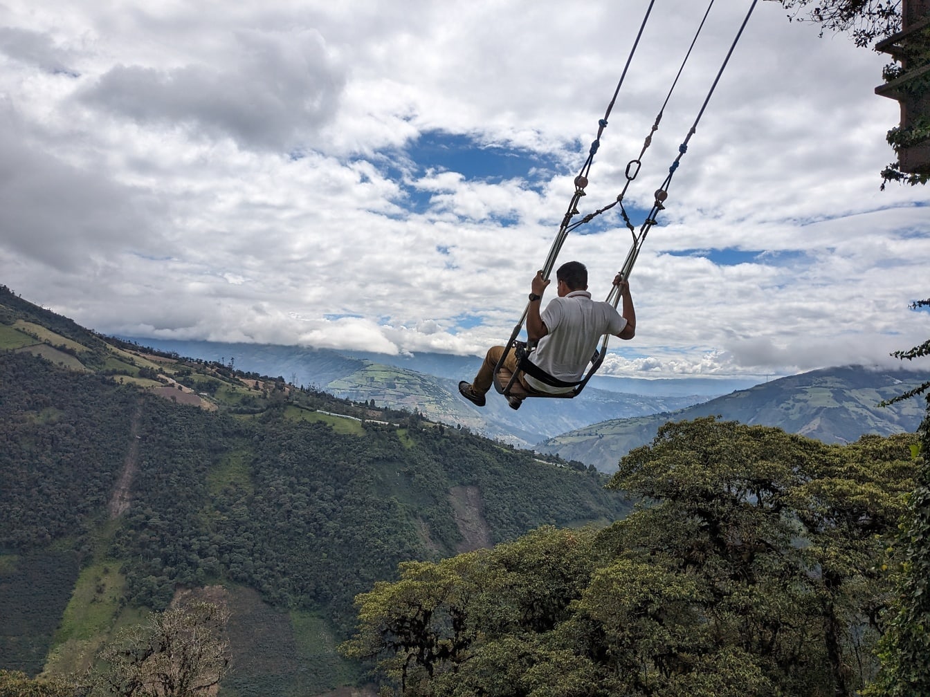 Homem extremamente corajoso balançando em um grande balanço sobre um vale na cidade de Banos, no Equador