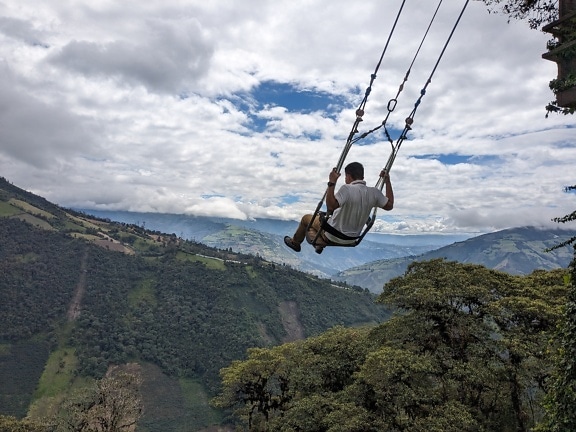 Extrem mutiger Mann, der auf einer großen Schaukel über einem Tal in der Stadt Banos in Ecuador schwingt