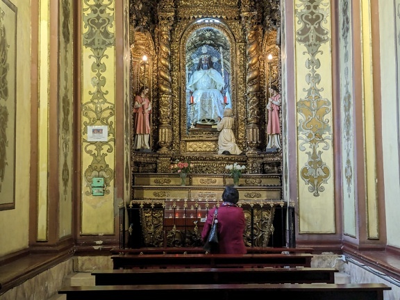 A woman praying at an ornate altar in a Catholic church in Latin America