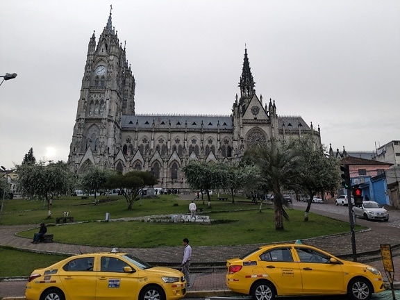 Due taxi gialli parcheggiati di fronte alla basilica neogotica cattolica romana del Voto Nacional con una torre dell’orologio a Quito, capitale dell’Ecuador