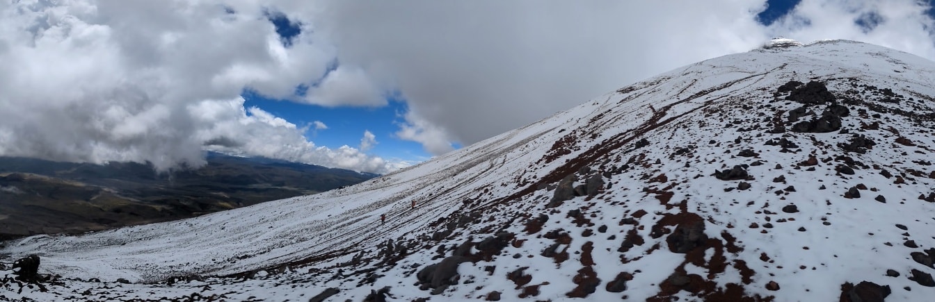 Gunung yang tertutup salju dengan orang-orang di kejauhan berjalan menaiki bukit