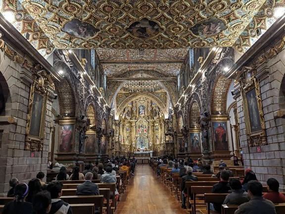 People sitting inside magnificent basilica and convent in baroque style of San Francisco in Quito, Ecuador
