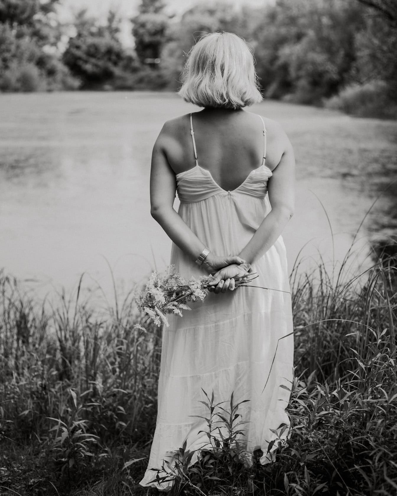 Svart-hvitt portrett av bruden vendt mot ryggen i en hvit ryggløs kjole som holder blomster