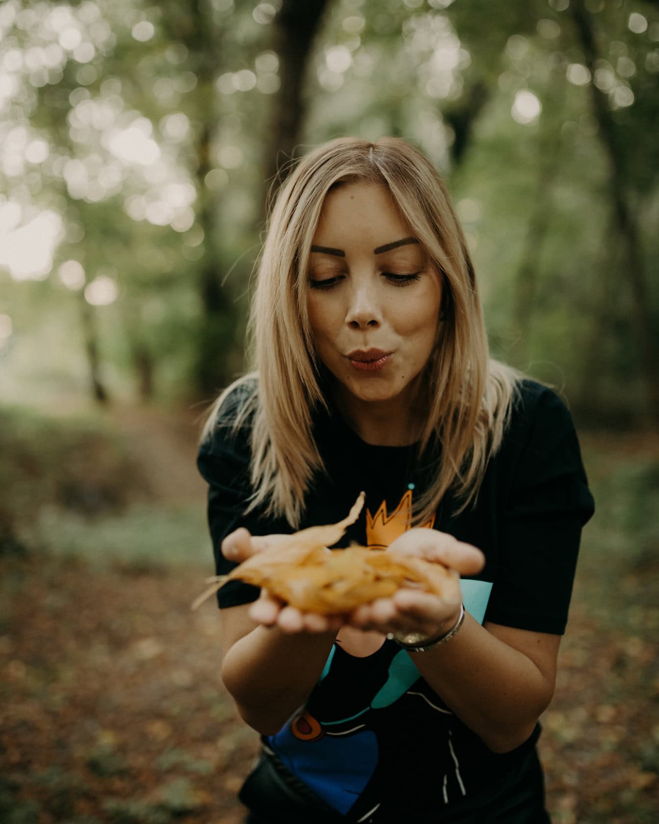Една жена държи сухи есенни листа в ръцете си и духа в нея
