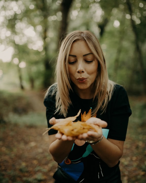 A woman holds dry autumn leaves in her hands and blows into it