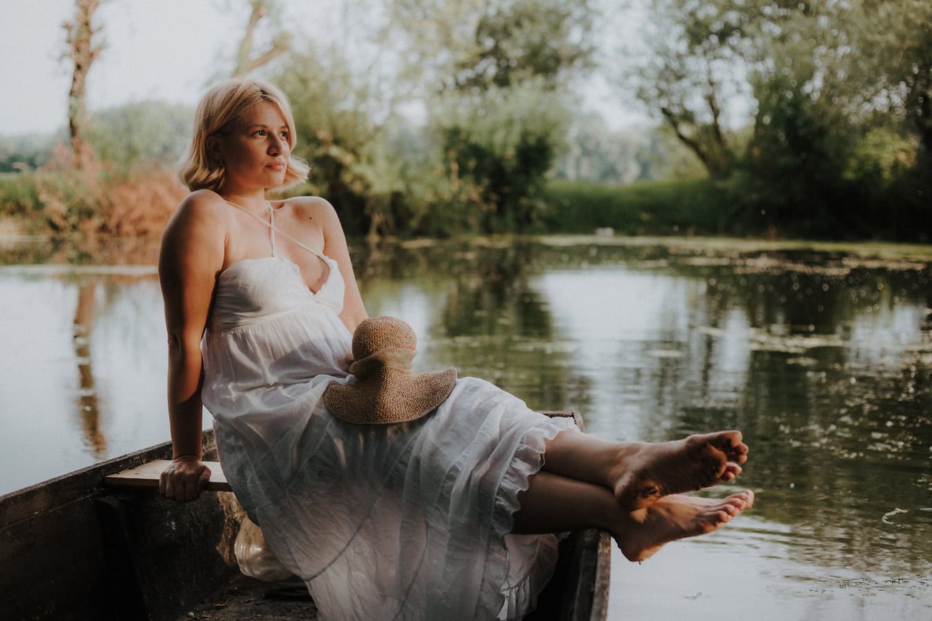 Potret pengantin wanita dengan wajah feminin halus dalam gaun putih duduk di atas perahu di air