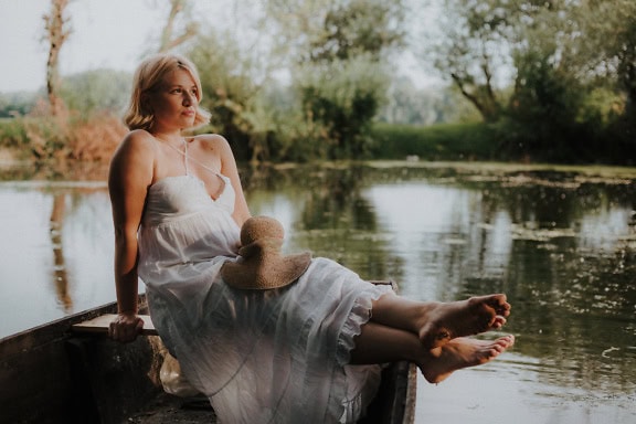 Porträt einer Braut mit zartem, weiblichem Gesicht in einem weißen Kleid, die auf einem Boot im Wasser sitzt