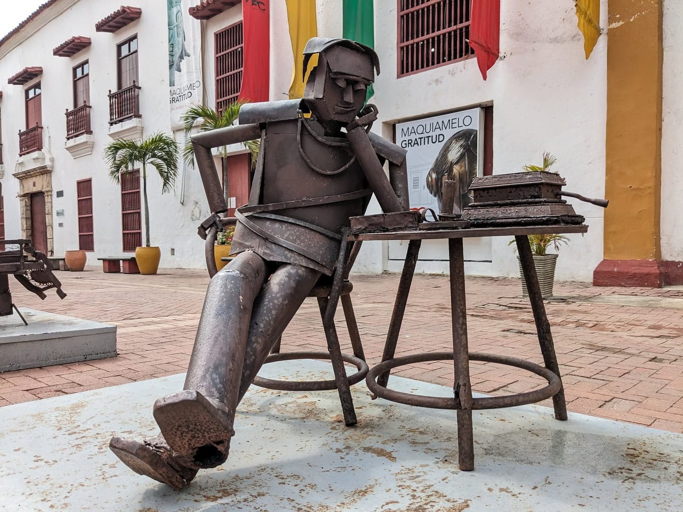 Patsas miehestä, joka istuu pöydän ääressä Plaza de los Cochesin aukiolla Cartagenassa, Kolumbiassa