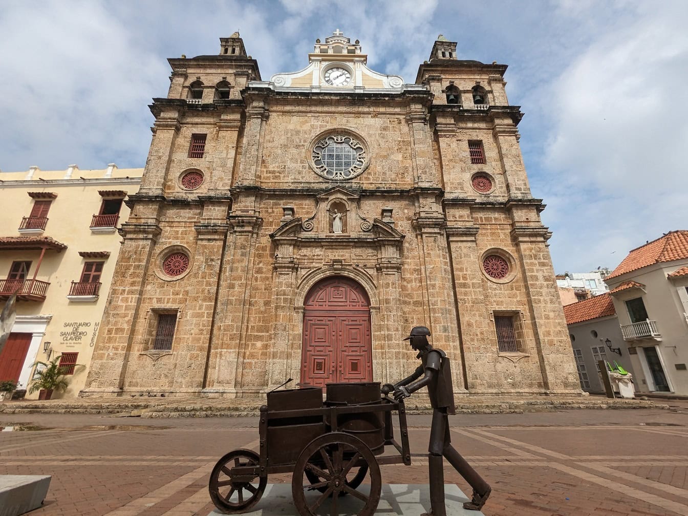 在哥伦比亚卡塔赫纳的圣佩德罗·克拉弗（San Pedro Claver）的殖民建筑风格的教堂前推着手推车的男人雕像