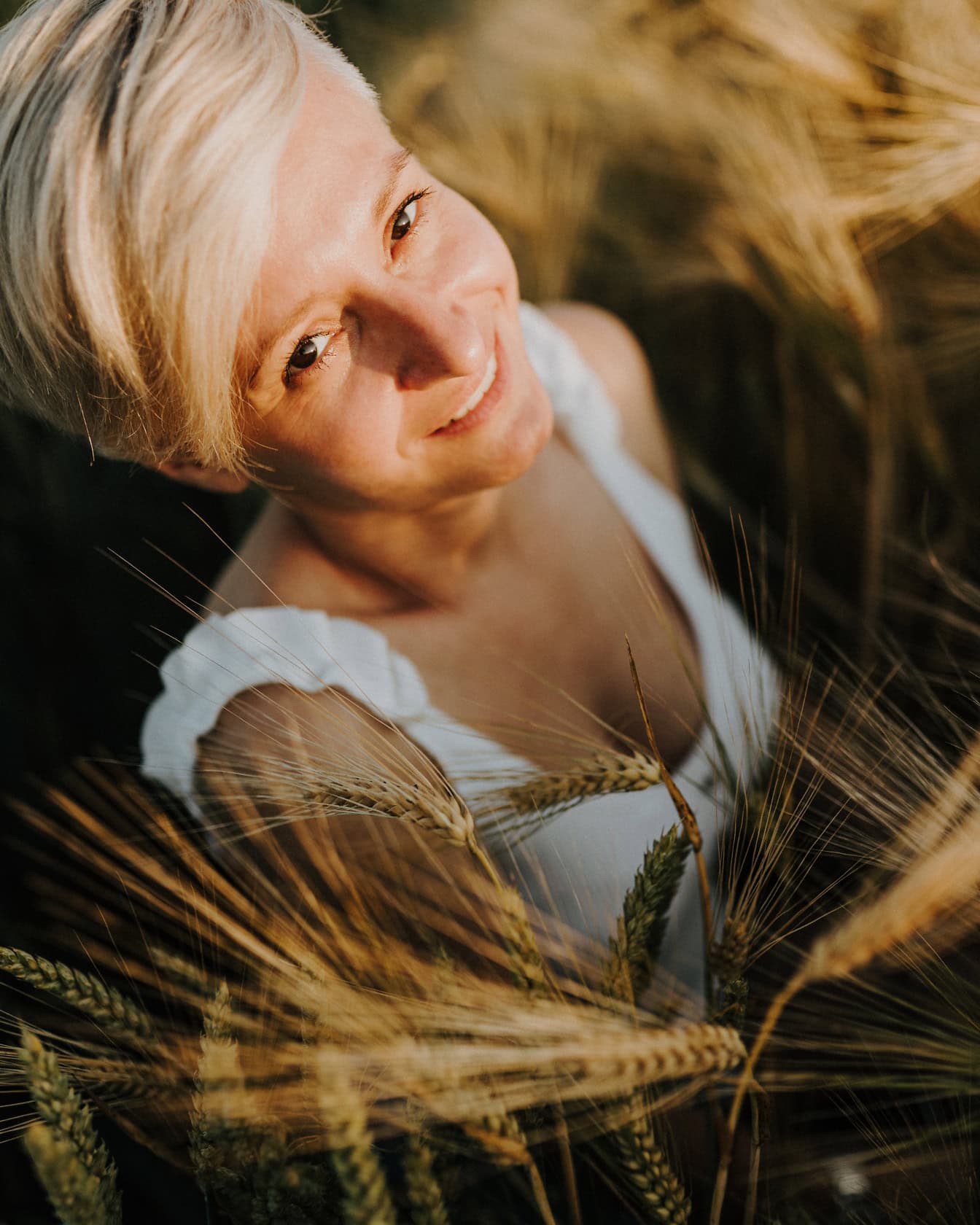 Potret close-up seorang pirang tersenyum dengan rambut pendek berpose di ladang gandum