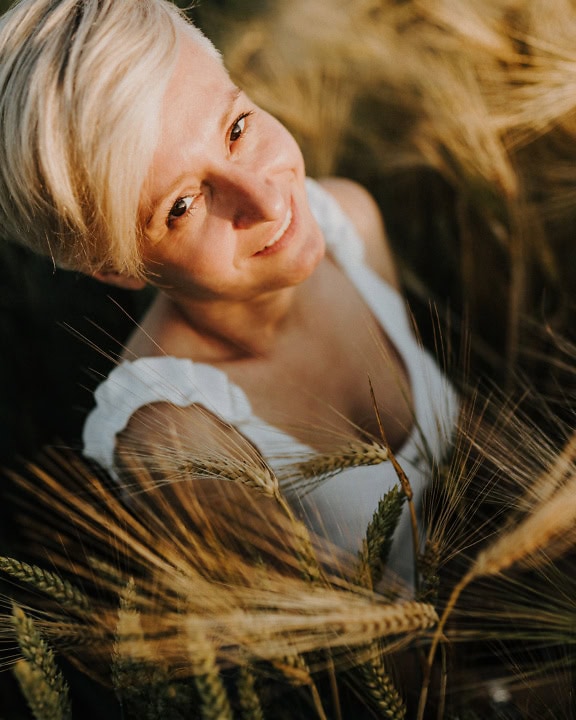 Портрет в близък план на усмихната блондинка с къса коса, позираща в житно поле