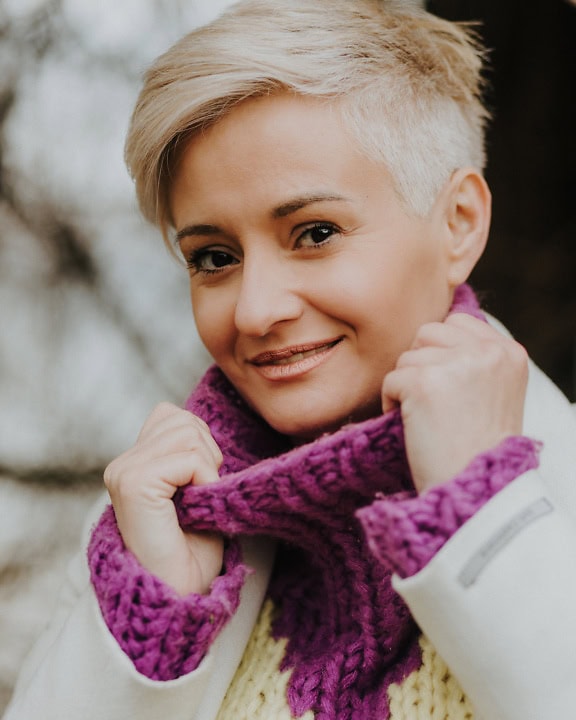 Woman with short blond hair and delicate eye-catching makeup on her face wearing a purple knitted wool sweater