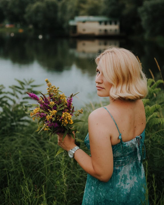 Portret van een vrouw in een backless kleding die over haar schouder kijkt terwijl ze bloemen in haar hand houdt