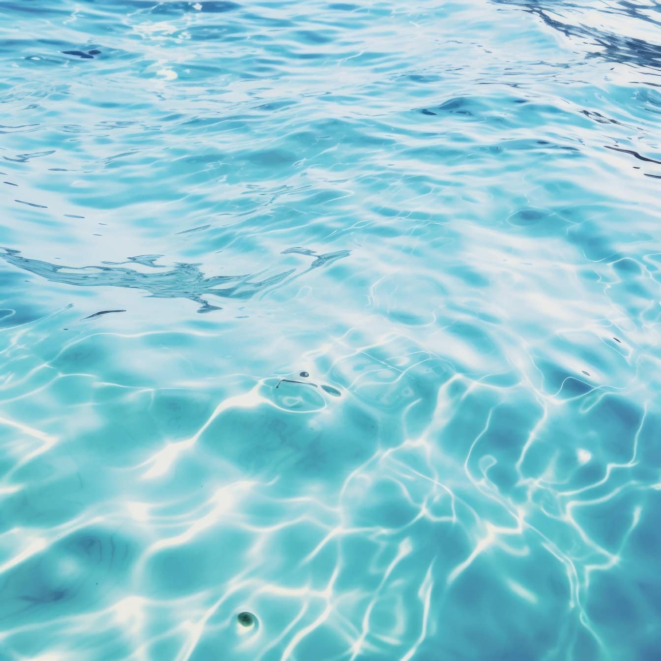 Klare, türkisblaue Wasseroberfläche mit Wellen und Reflexion der Sonnenstrahlen