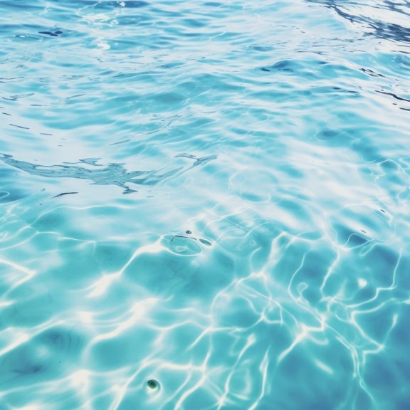 Suprafață limpede de apă albastră turcoaz cu ondulații și reflexie a razelor solare