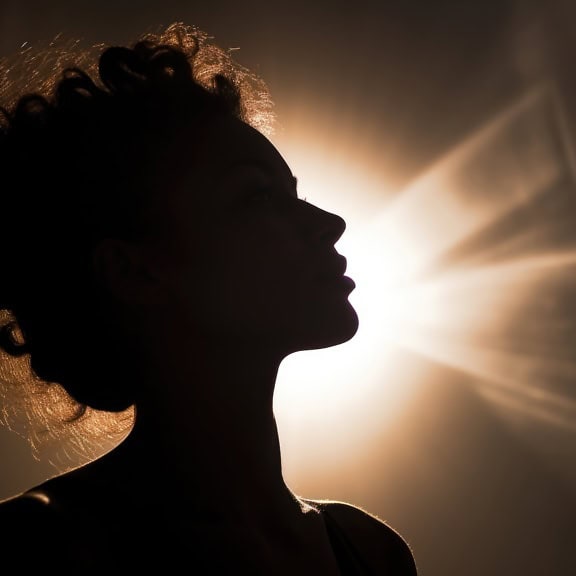Egy nő profiljának sziluettje, akinek a haján keresztül süt a Nap
