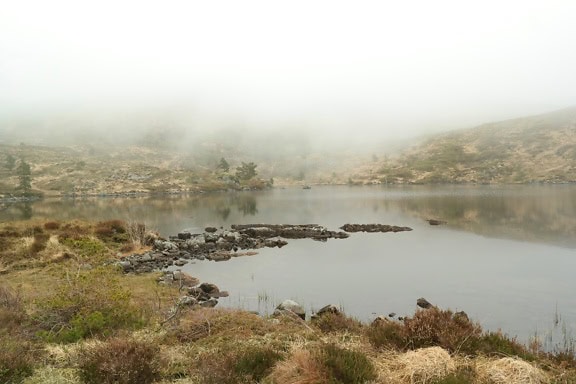 Thick white fog over the calm Scandinavian mountain lake