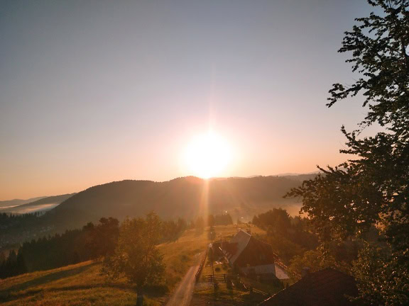 Soarele apune peste vale cu razele strălucitoare deasupra unei case rurale din munții Balcanilor