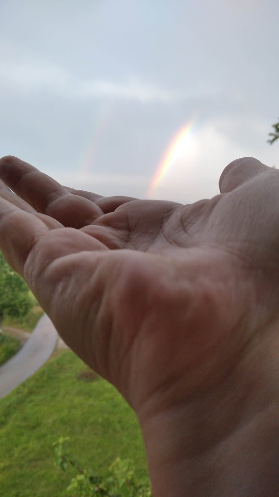 Close-up van de hand met een regenboog op de achtergrond die de illusie van een regenboog in de palm van hand creëert