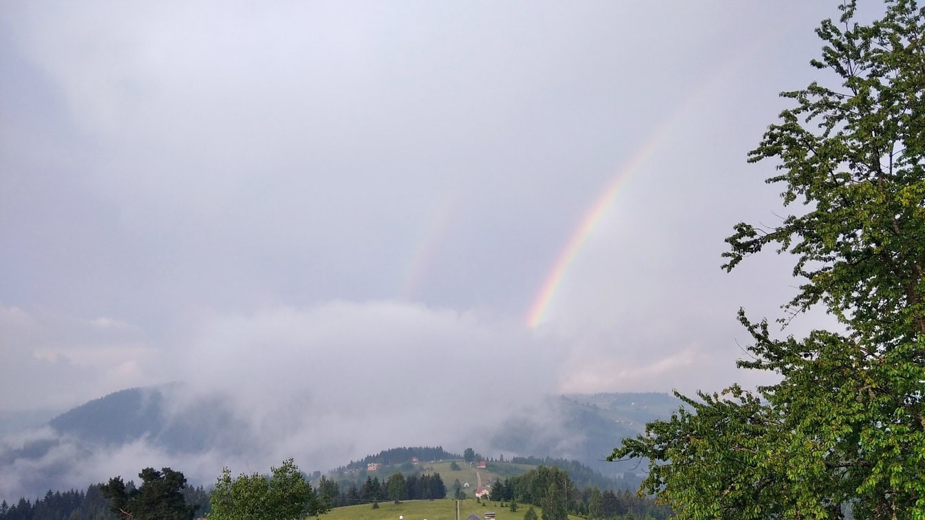 Regenbogen in weißen Wolken über einem Tal