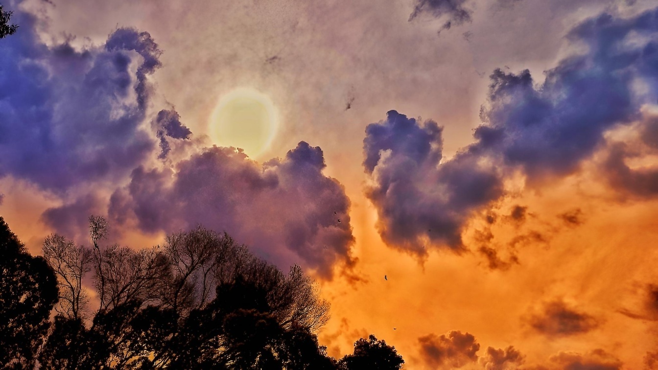 Słońce prześwitujące przez purpurowe chmury na pomarańczowo-żółtym niebie