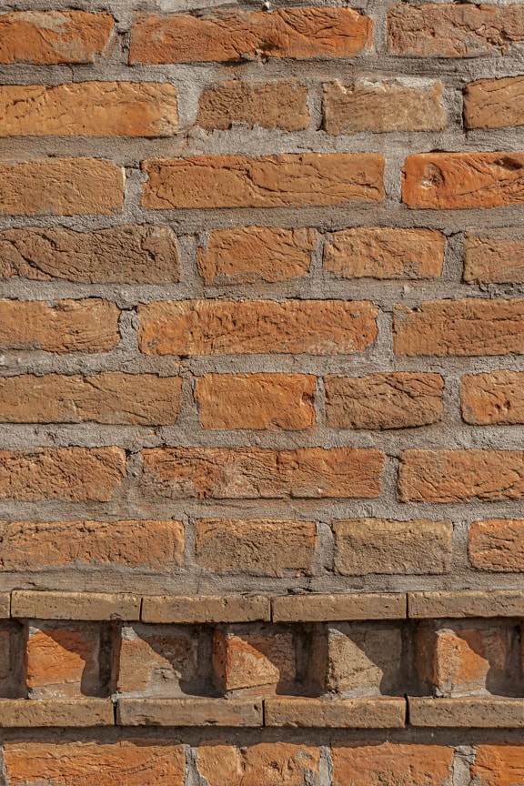 Textura de pared de ladrillo con gruesa capa de cemento entre ladrillos de gran formato y con cenefa decorativa horizontal en la parte inferior