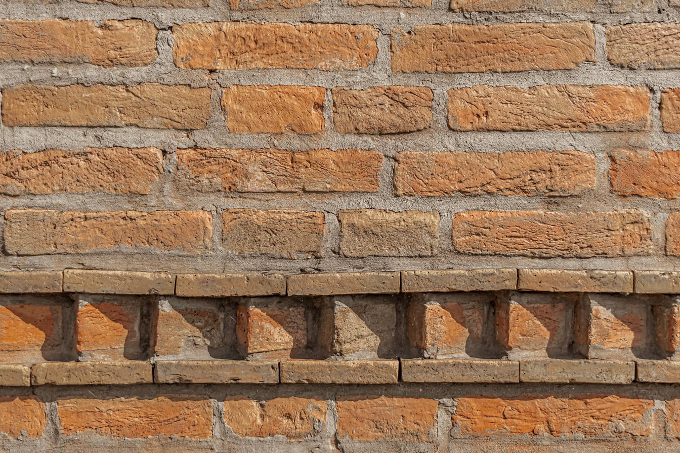 Parede de tijolo velho com camada de cimento grosso entre tijolos empilhados horizontalmente e com borda decorativa no fundo