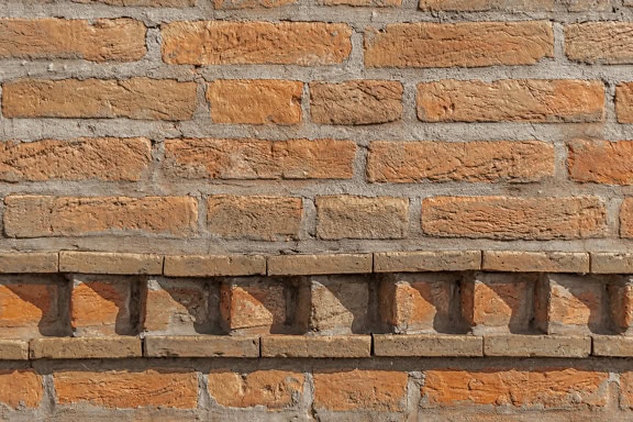 Gammel murvegg med tykt sementlag mellom horisontalt stablede teglstein og med dekorativ kant nederst