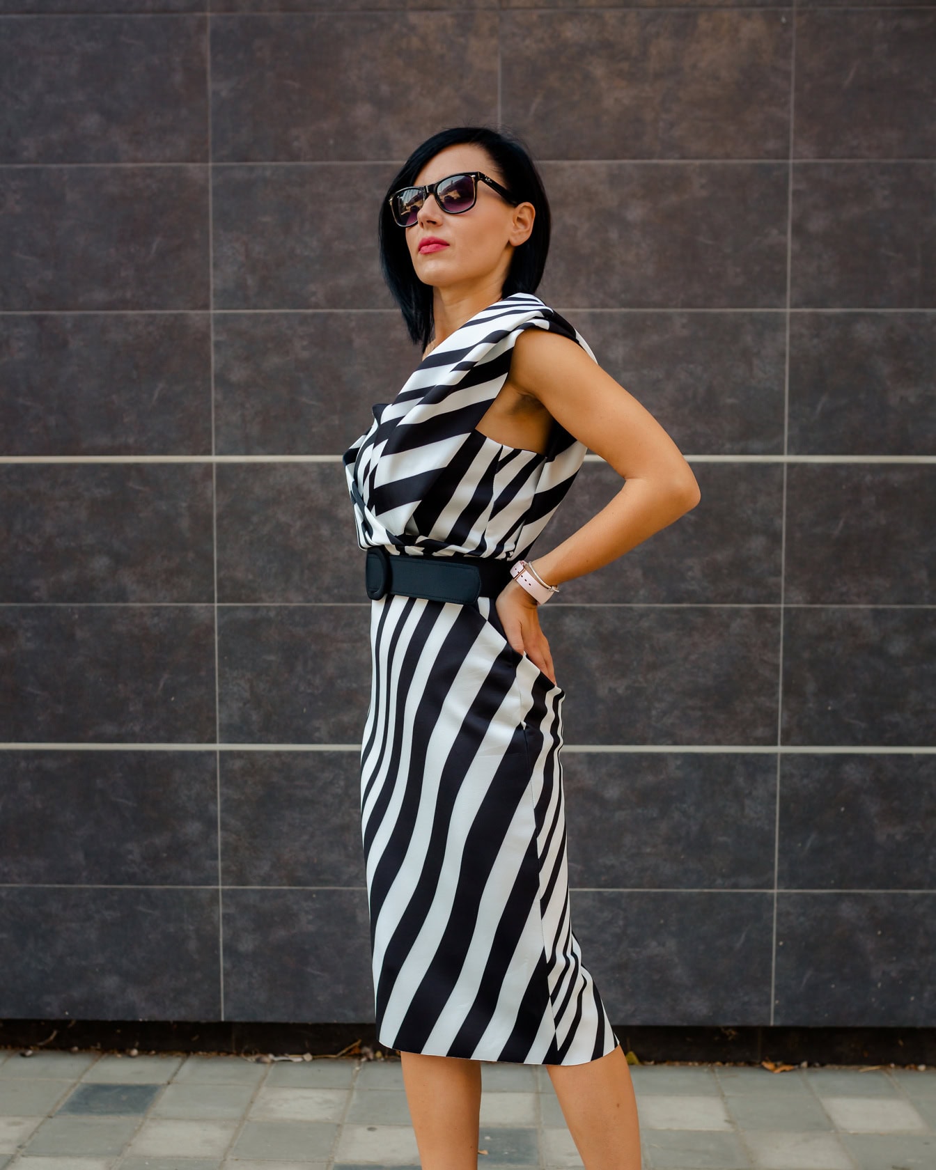 Selvsikker pen forretningskvinne poserer i en svart og hvit stripete kjole med svart belte mens iført solbriller