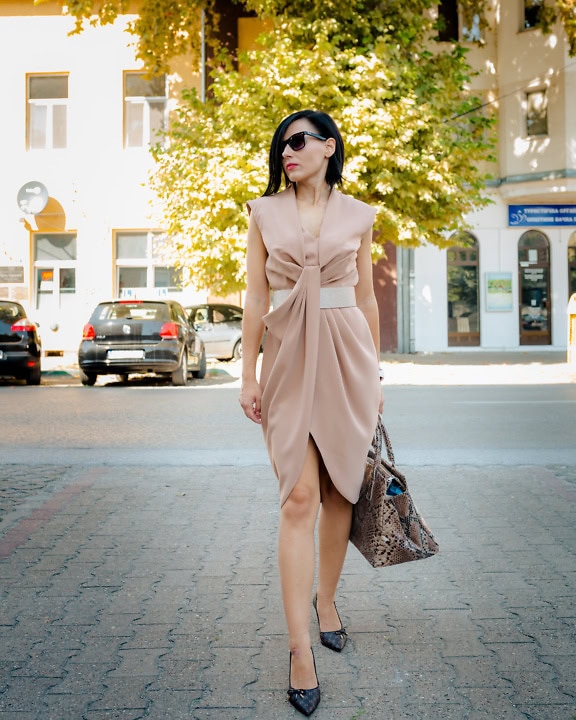 Gut aussehende Geschäftsfrau in einem eleganten beigen Kleid geht die Straße entlang