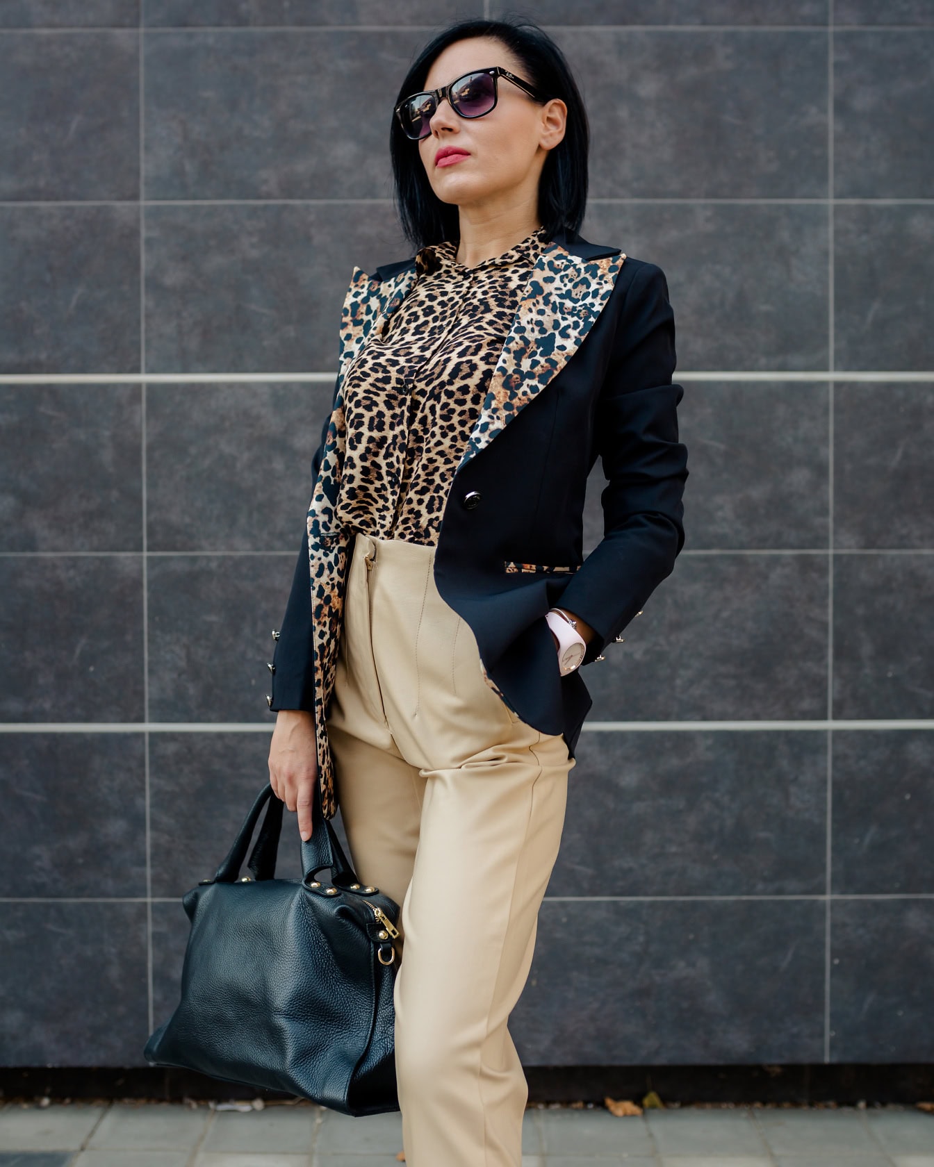 Pengusaha wanita berpose dalam kemeja motif macan tutul dan celana cokelat dengan tas kulit hitam