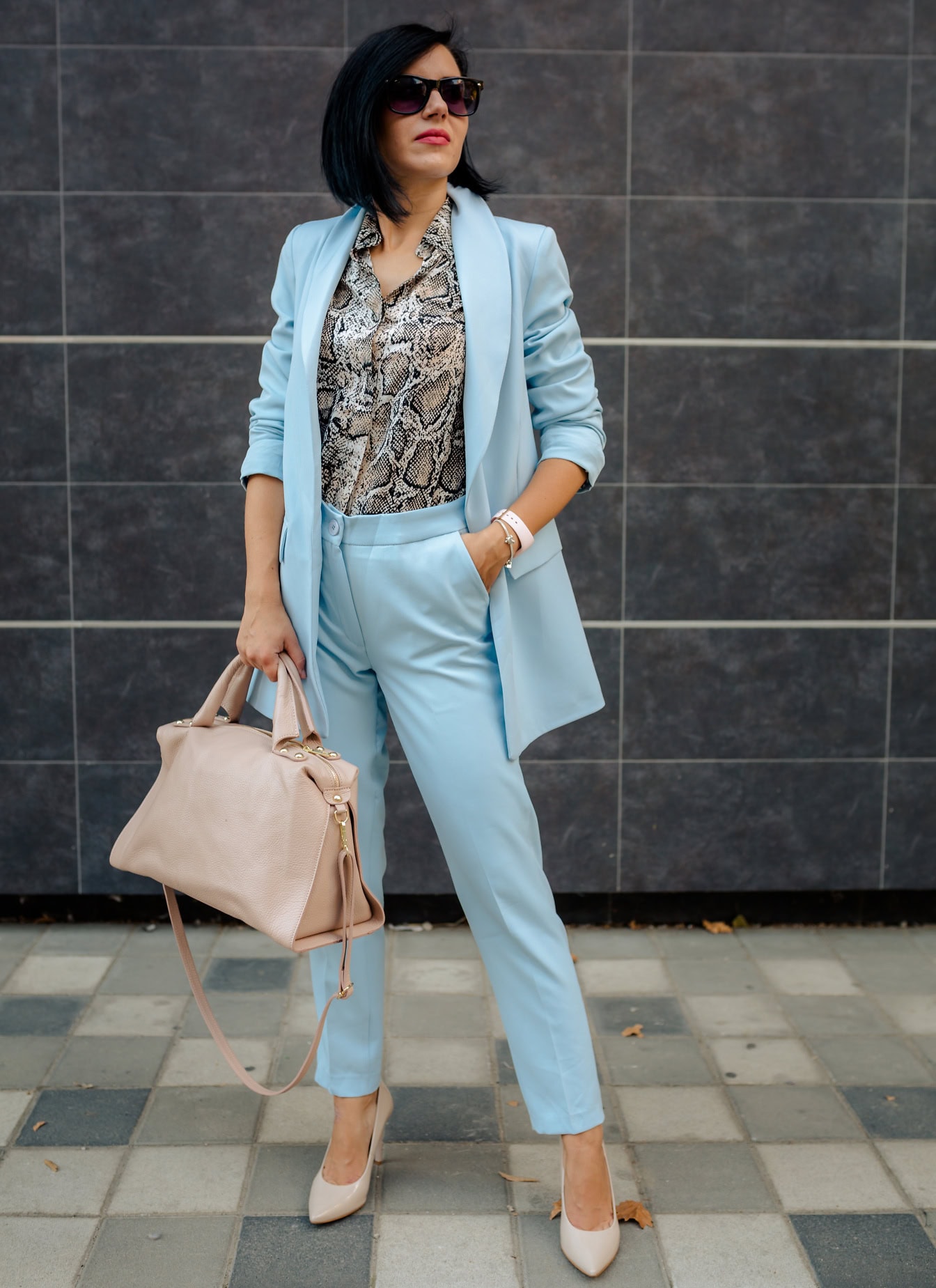 Gut aussehende Geschäftsfrau posiert in einem blauen Anzug mit Hemd mit Schlangenmuster und Sonnenbrille