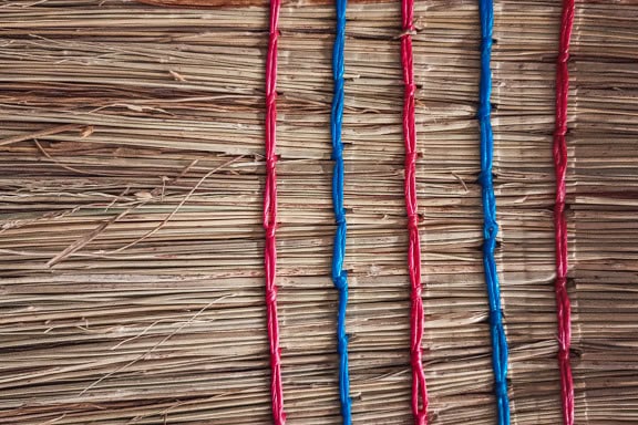 Detail textury povrchu slaměného koštěte s tmavě červenými a modrými nylonovými strunami