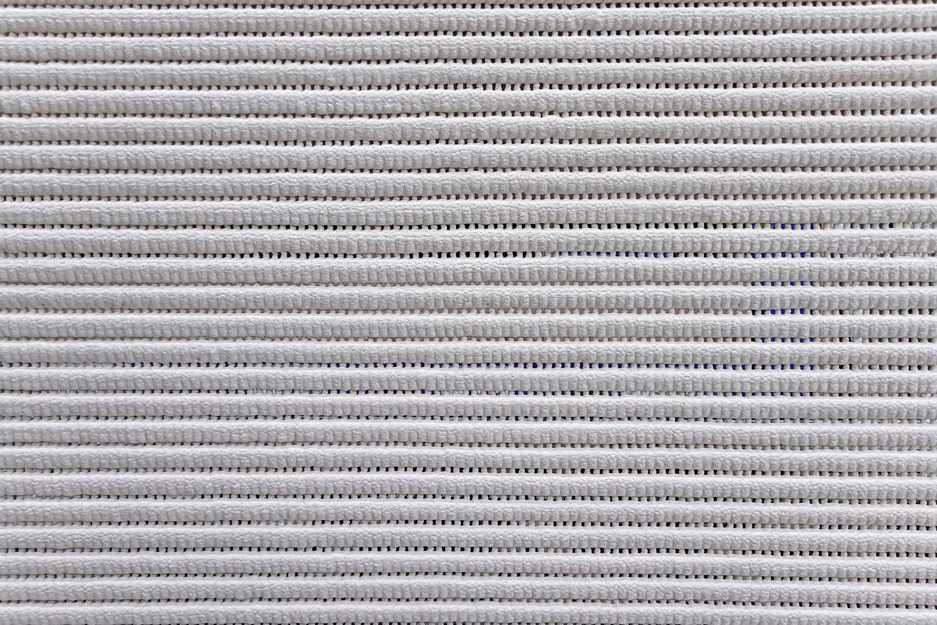 Tekstur af et gråhvidt svampestof med små linjer lavet af huller