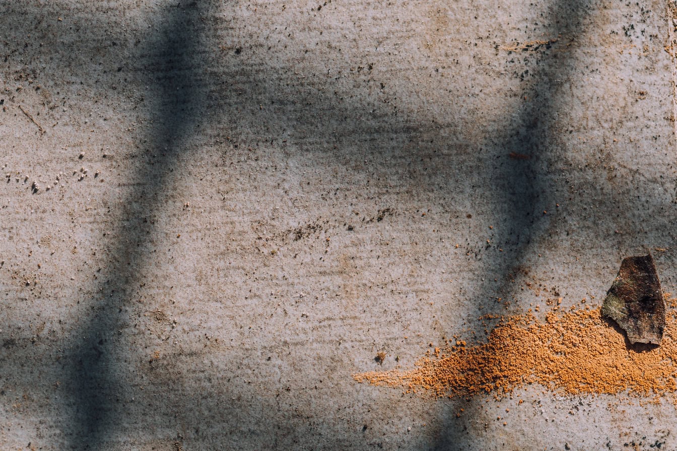 Close-up texture of of a dirty cement surface in shadow with orange-yellow powder on it