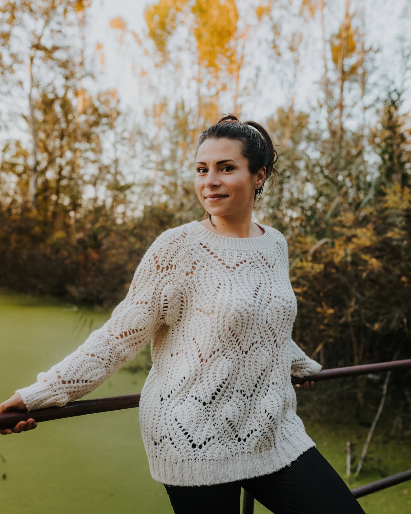 Brunette cantik dengan riasan bijaksana dalam sweter putih buatan tangan saat dia bersandar di pagar jembatan di seberang kanal