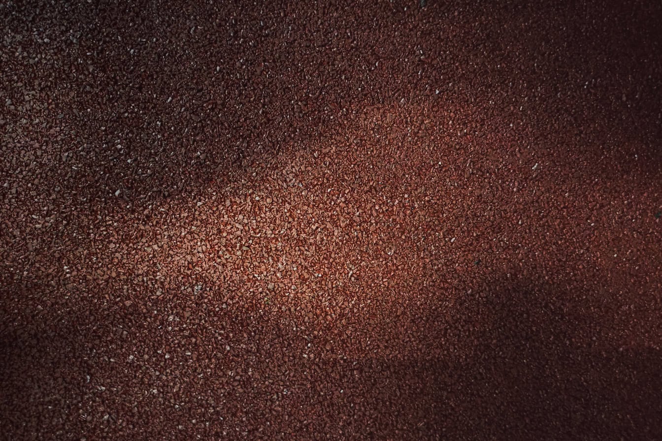 Textur av mörkt rödbrun gummiyta gjord av återvunnet gummi i skugga