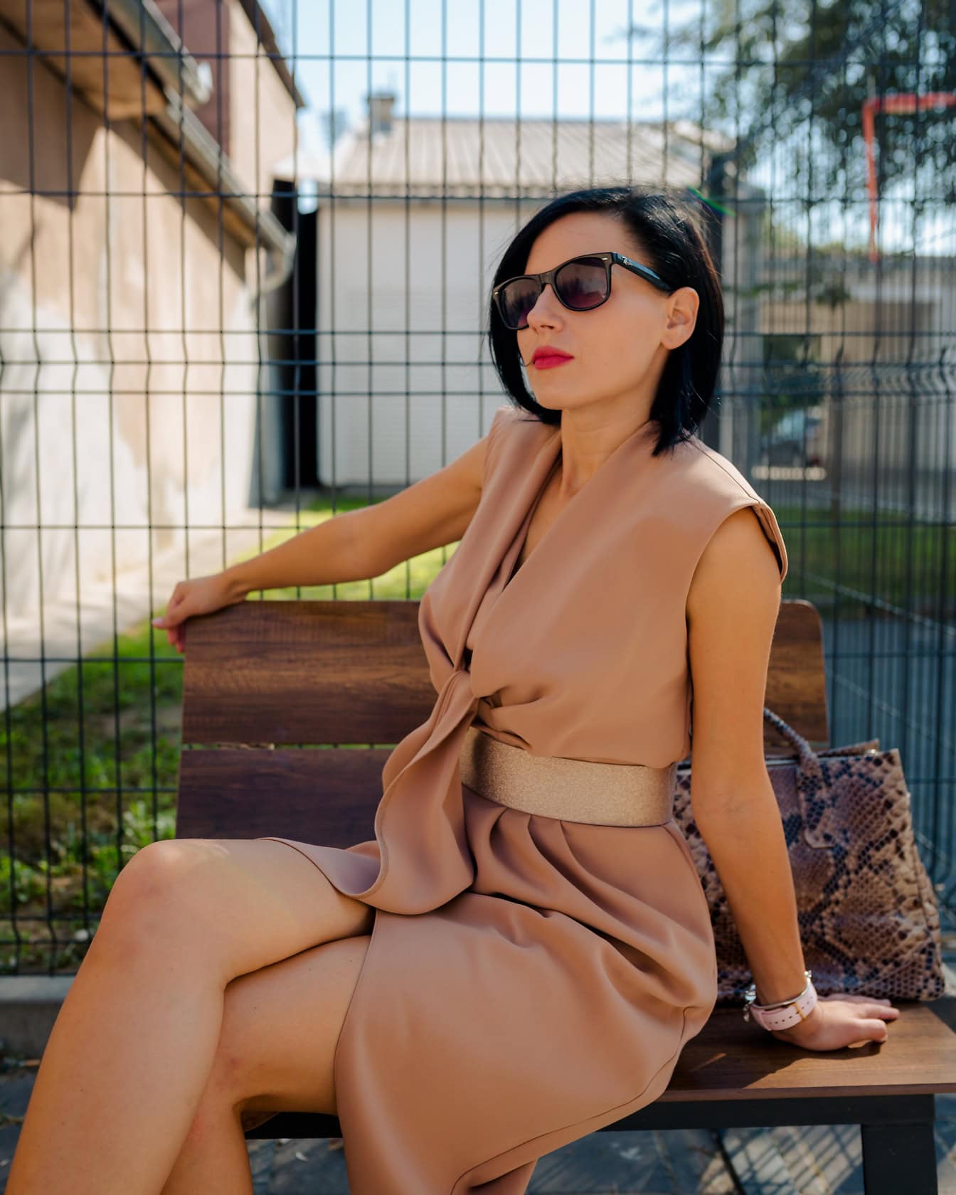 Donna seduta e prendere il sole su una panchina in abito brunastro pastello con cintura lucida in vita