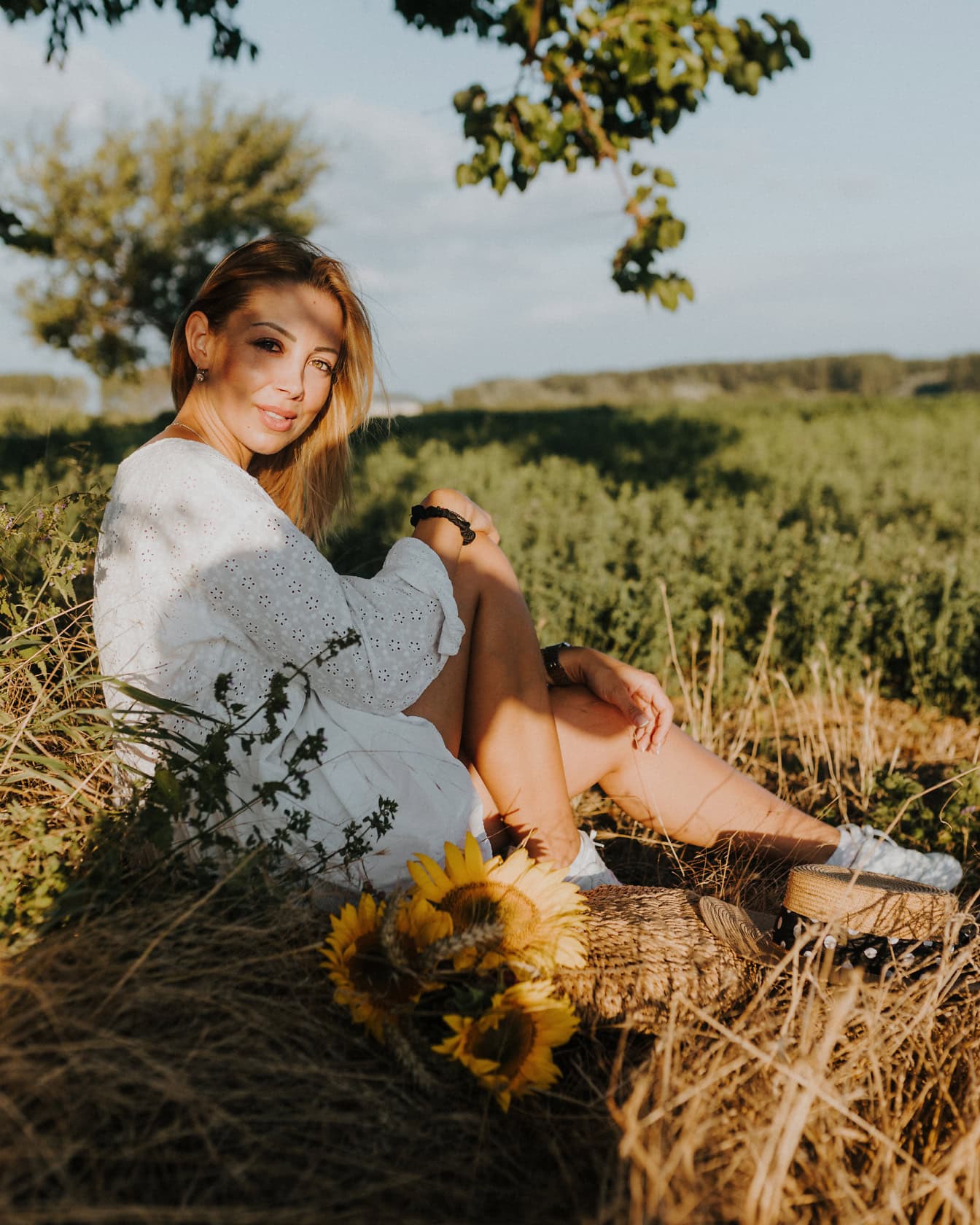 Потрясающе красивая деревенская девушка сидит в поле под деревом в полутени