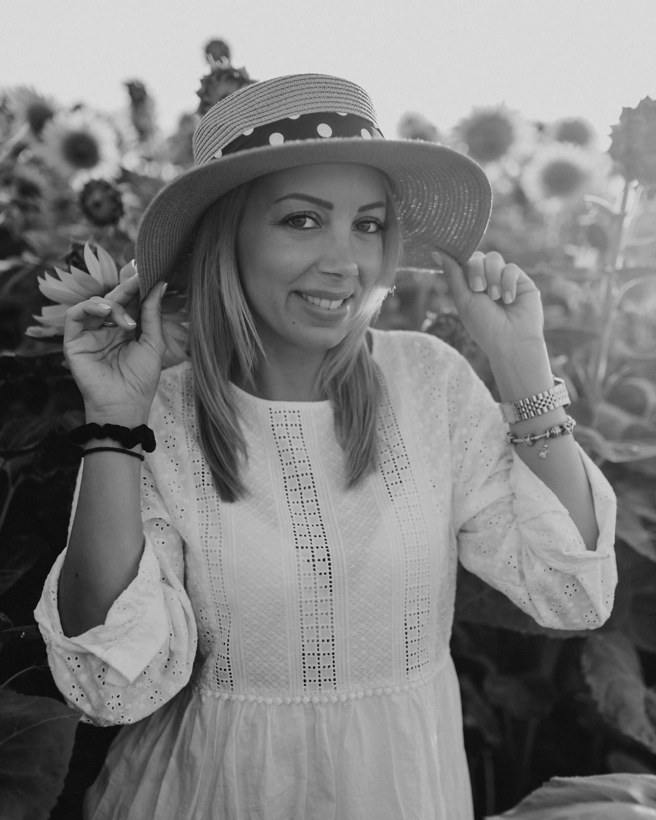 Sort-hvidt portræt af en smuk smilende cowgirl iført stråhat i en solsikkemark
