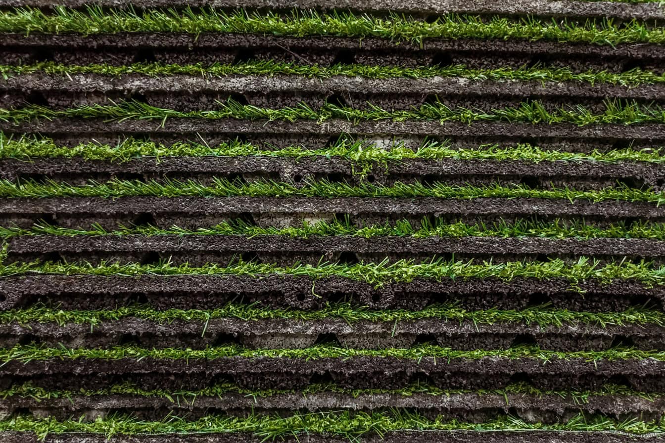 Tekstur rumput sintetis yang terbuat dari karet lateks daur ulang dan alami yang ditumpuk secara horizontal di atas satu sama lain