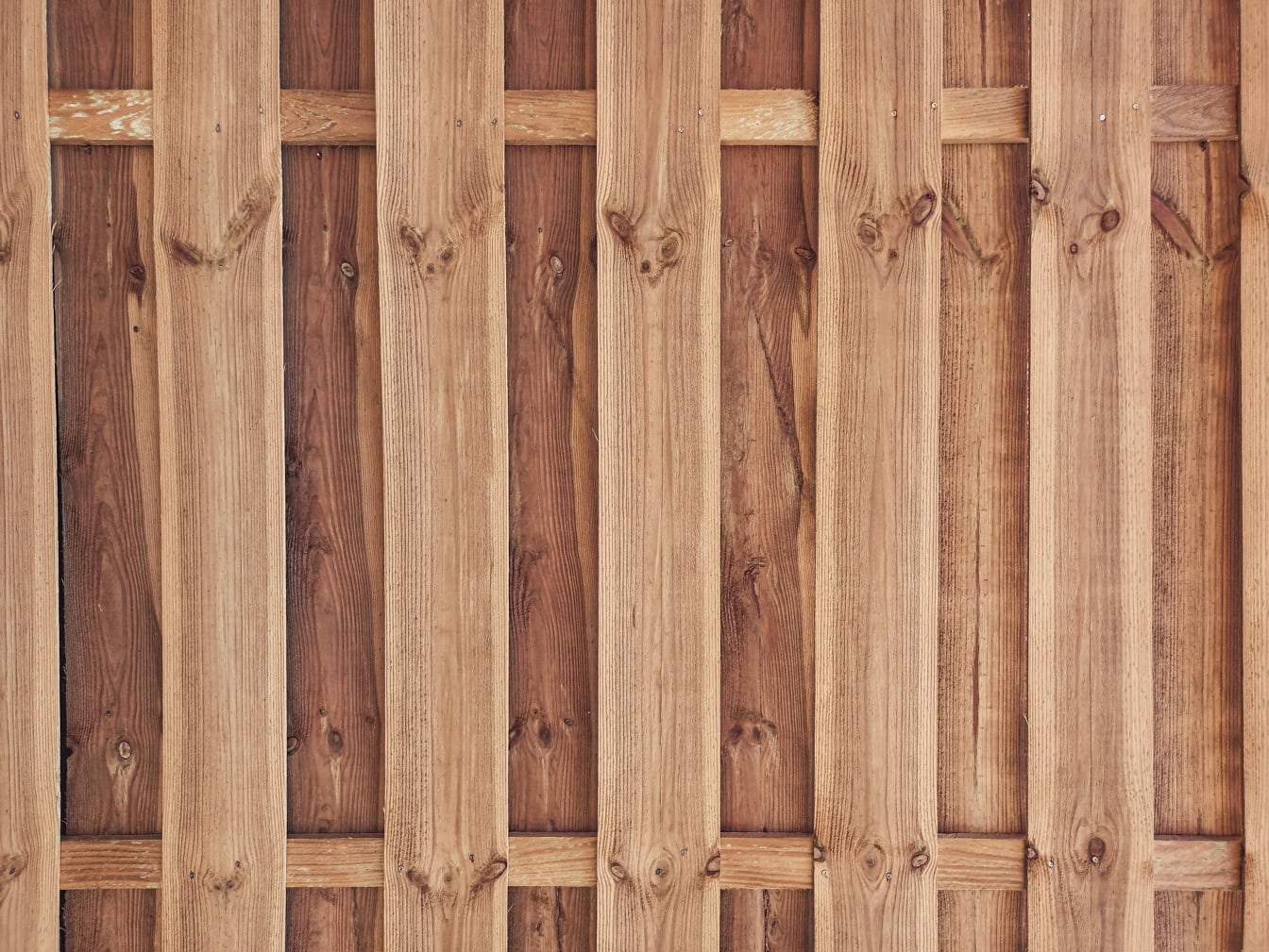 A lumber panel made out of vertically stacked hardwood slats in a form of picket fence with background made of planks with knots