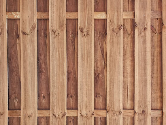 Et tømmerpanel laget av vertikalt stablede trelister i form av stakittgjerde med bakgrunn laget av planker med knuter